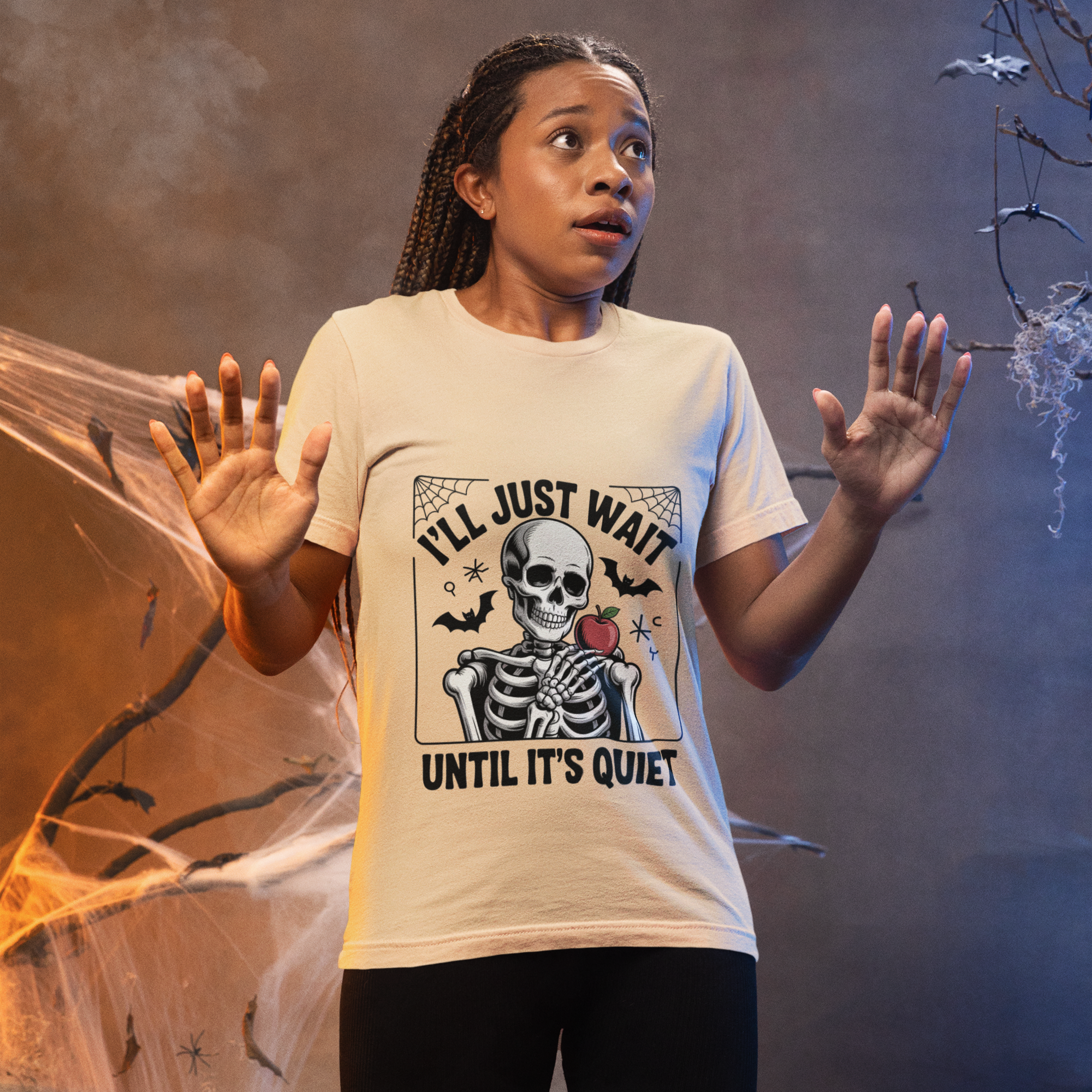 Woman wearing a cute beige Halloween teacher t-shirt with a skeleton design and the phrase “I’ll Just Wait Until It’s Quiet.