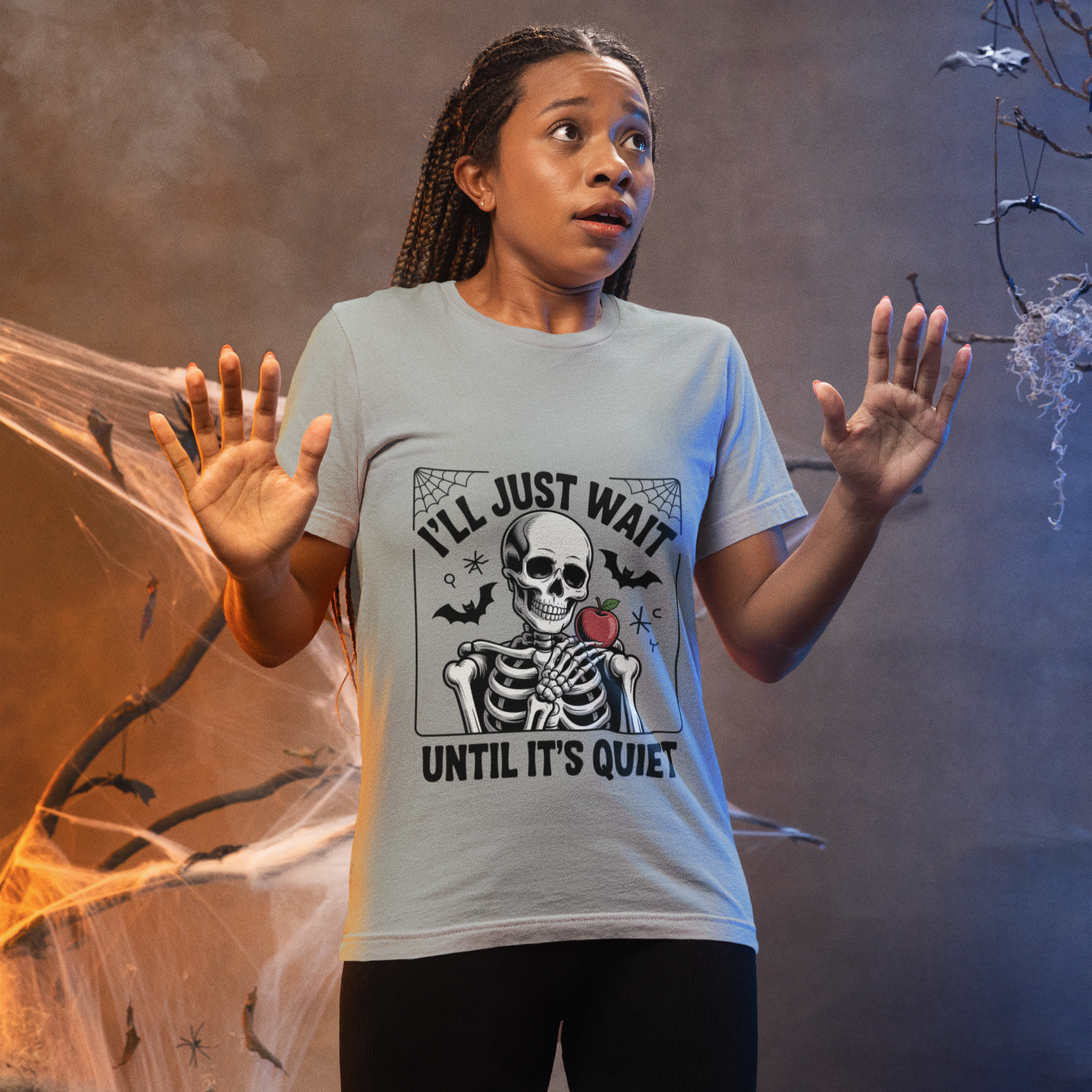 Woman wearing a cute gray Halloween teacher t-shirt with a skeleton design and the phrase “I’ll Just Wait Until It’s Quiet.