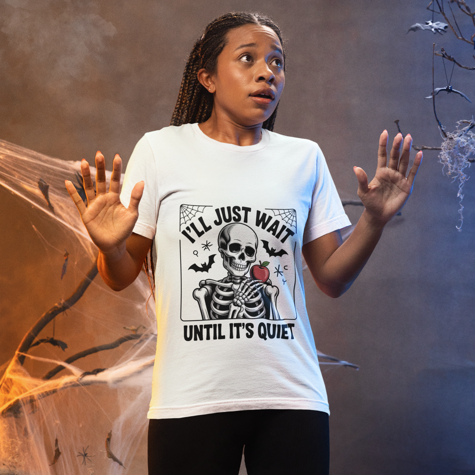 Woman wearing a cute white Halloween teacher t-shirt with a skeleton design and the phrase “I’ll Just Wait Until It’s Quiet.