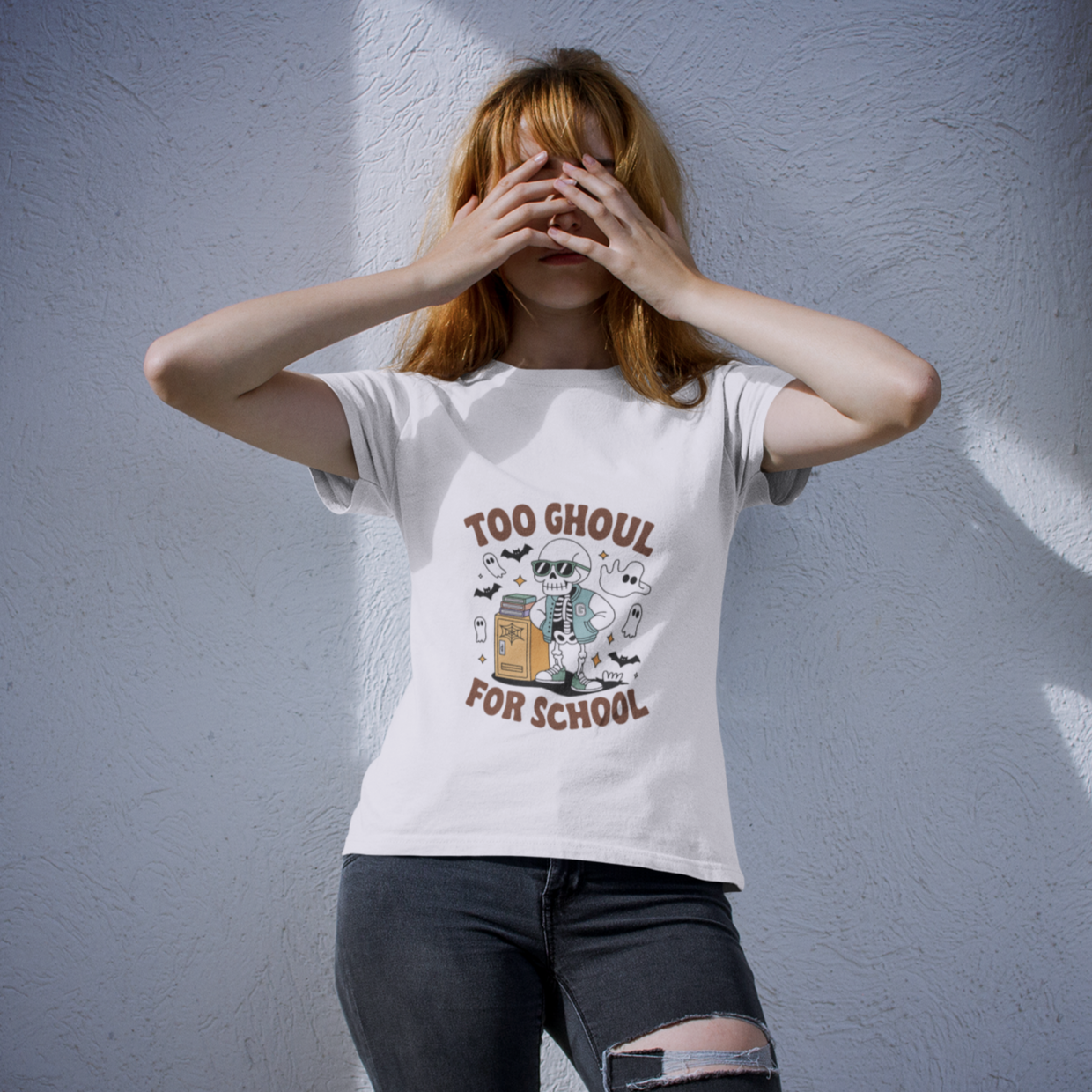 Person wearing a white fall t-shirt with a skeleton graphic and the phrase 'Too Ghoul for School