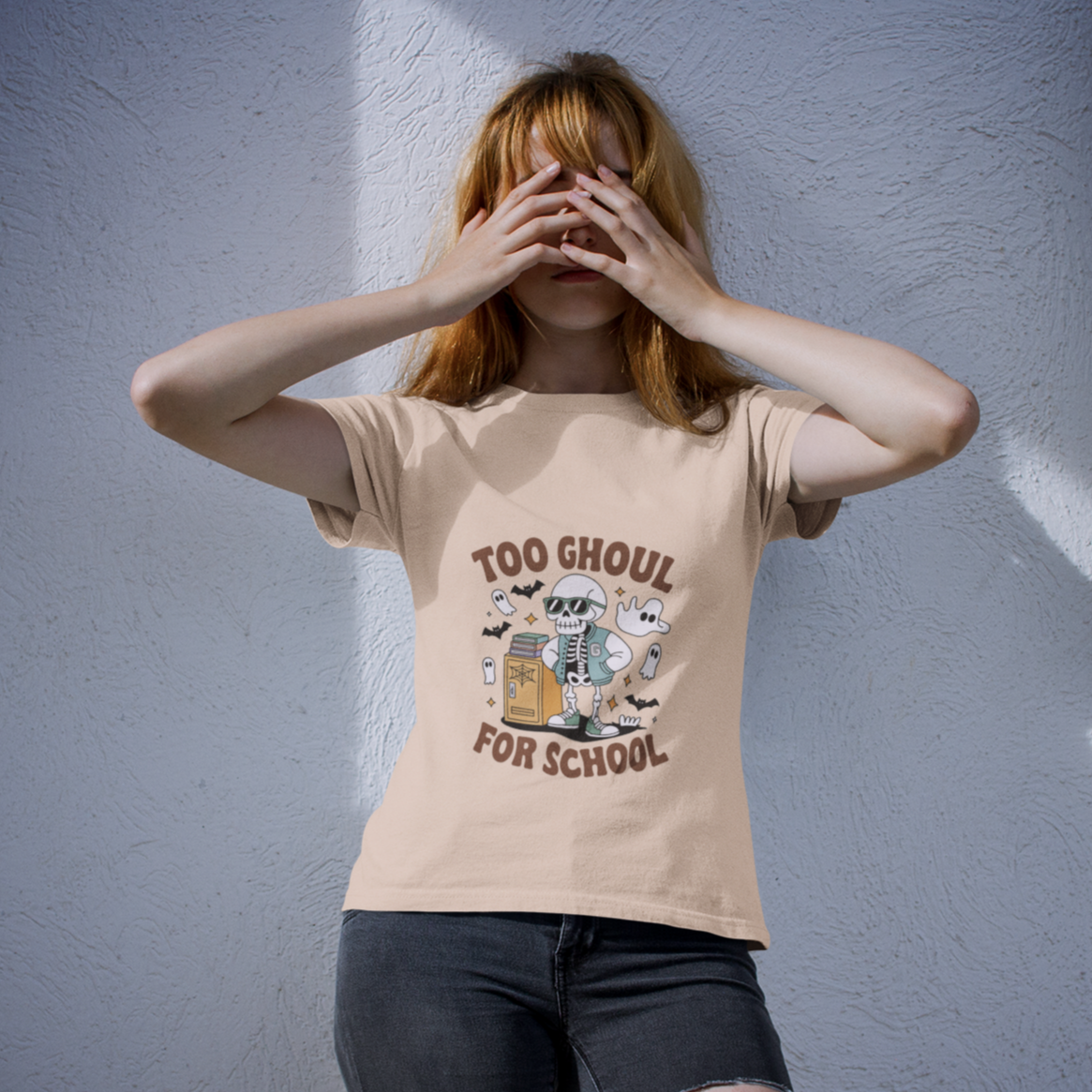Person wearing a beige fall t-shirt with a skeleton graphic and the phrase 'Too Ghoul for School