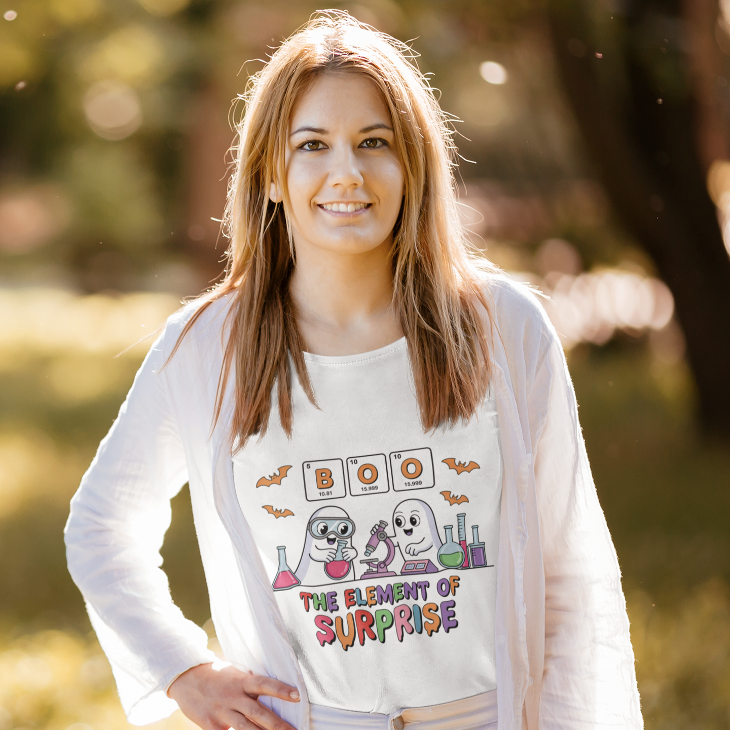 Woman wearing a white t-shirt with the phrase “Boo! The Element of Surprise,” featuring a science-themed Halloween design