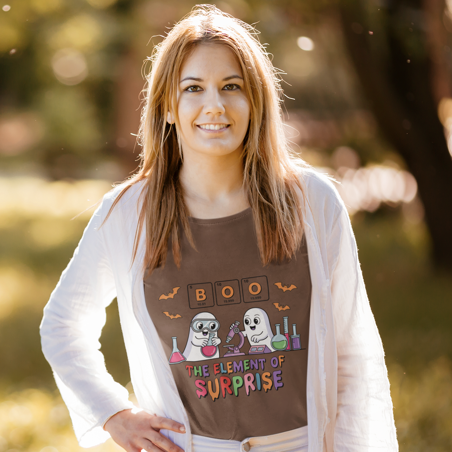 Woman wearing a brown t-shirt with the phrase “Boo! The Element of Surprise,” featuring a science-themed Halloween design