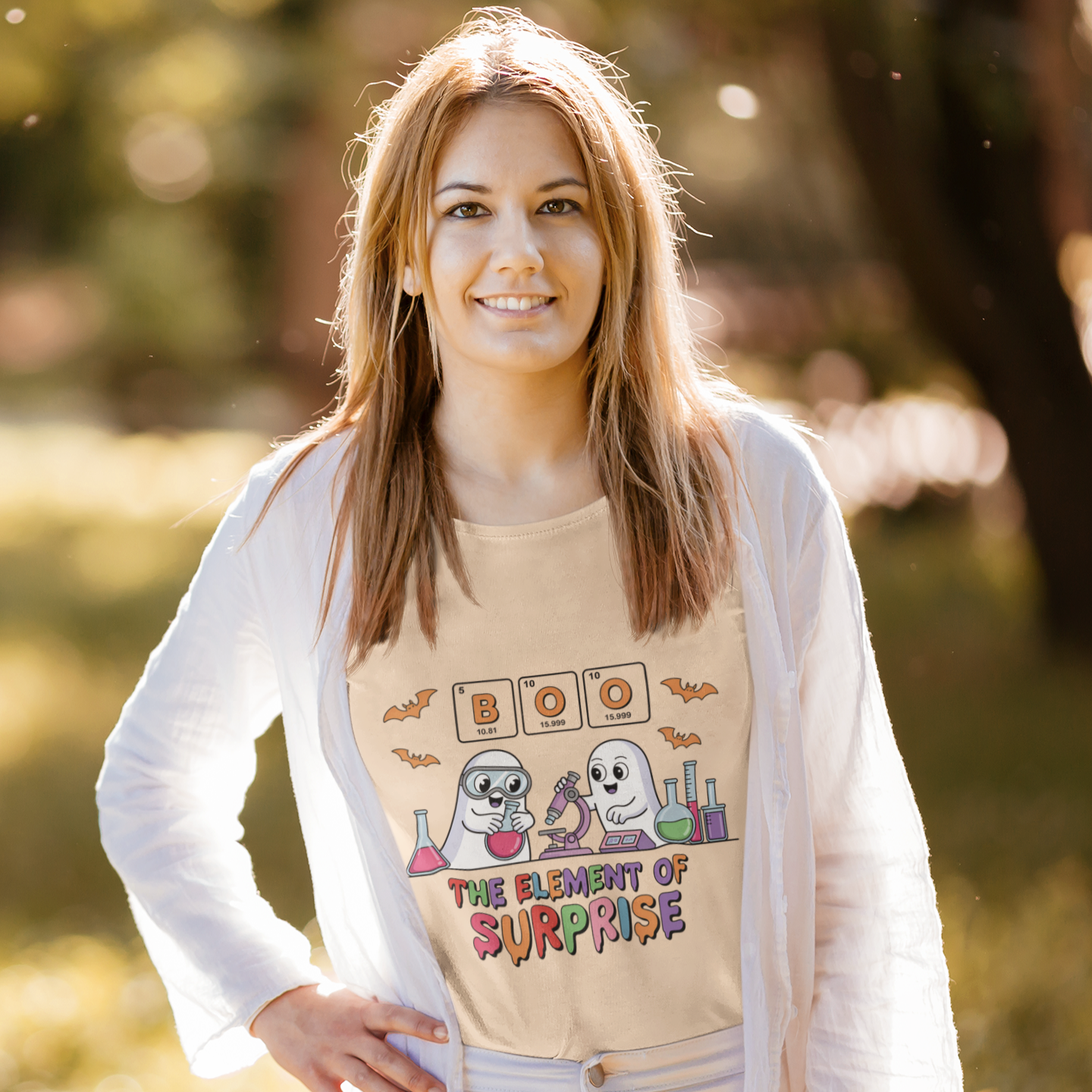 Woman wearing a beige t-shirt with the phrase “Boo! The Element of Surprise,” featuring a science-themed Halloween design