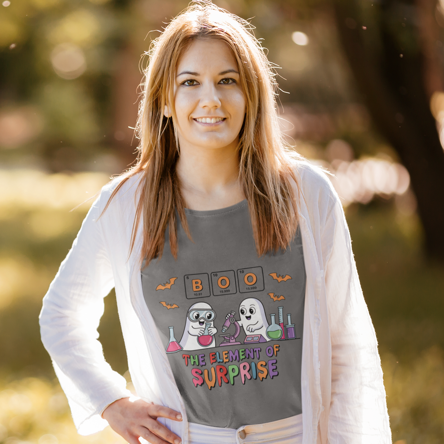 Woman wearing a gray t-shirt with the phrase “Boo! The Element of Surprise,” featuring a science-themed Halloween design